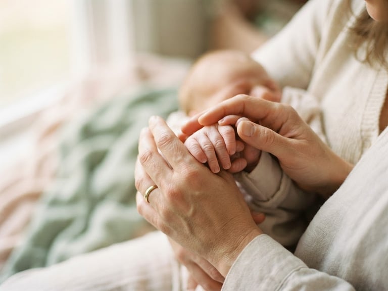 A close-up of a parent's hands gently holding a baby's hands, in soft natural morning light, gentle pastel tones, shallow depth of field, 35mm. The focus is on the warmth and care of the hands, with a blurred background.