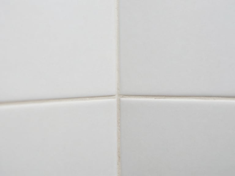 Close-up macro shot of perfectly aligned large format white tiles with minimal grout lines in a modern bathroom, showcasing impeccable mitered edges where two surfaces meet. Sharp focus on texture and precision.