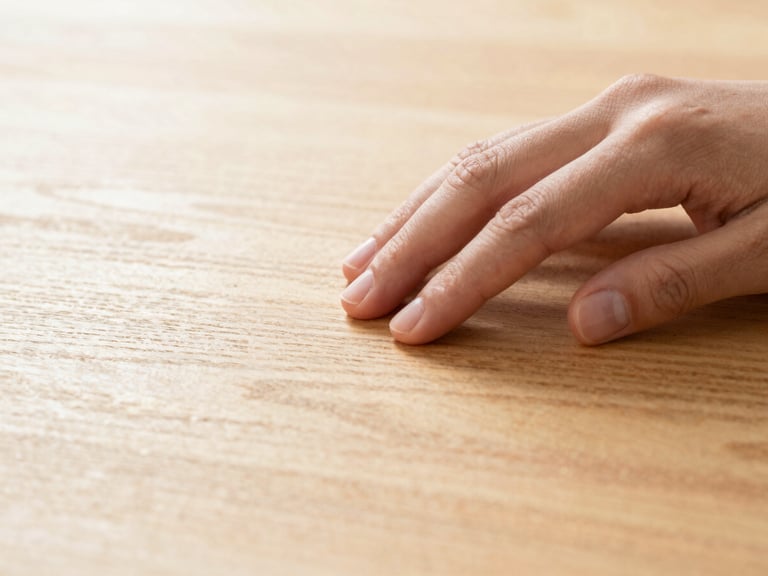Macro shot of a hand gently running over a polished, dust-free wooden surface, golden light catching the grain, immaculate detail.
