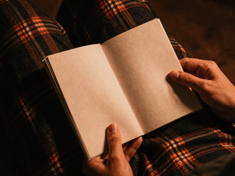 A warm-toned close-up of textured heavy flannel fabric and hands holding an old independent zine, low-key lighting, copper and charcoal color palette, atmospheric film texture