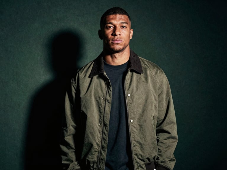 Low-key dramatic portrait of a modern footballer in high-fashion streetwear, cinematic shadows, desaturated tones, 35mm grain.