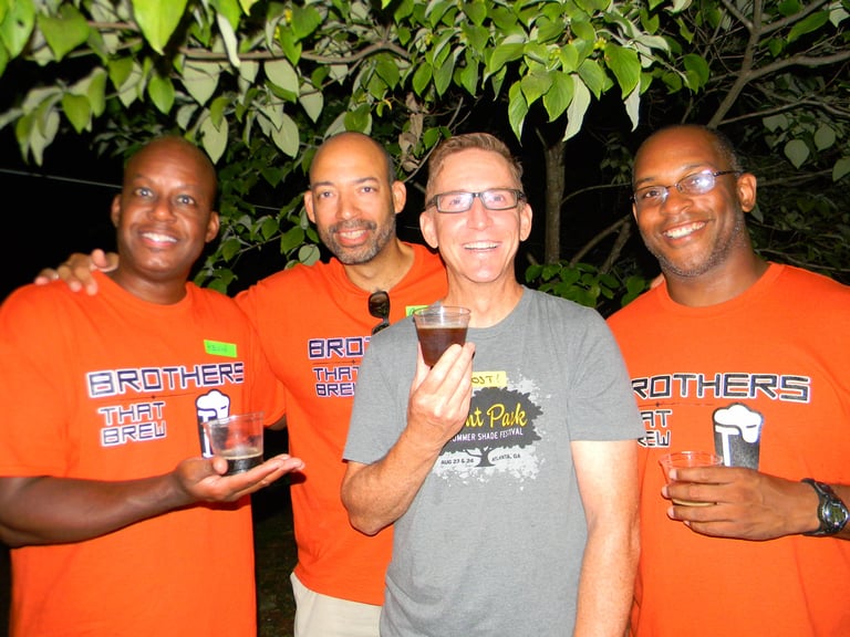 Four men smiling, wearing Brothers That Brew shirts and holding small tasting glasses.