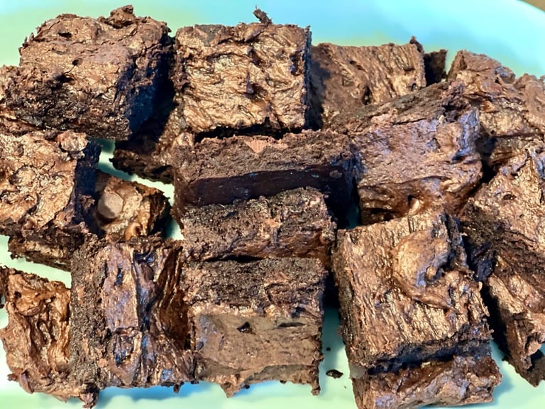 A close-up pile of homemade fudgy chocolate brownies with a crackly top on a light blue plate.