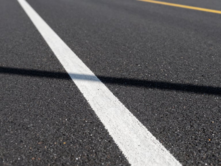 Low-angle 35mm perspective shot following a freshly painted crisp white line on dark asphalt, crisp morning sun casting sharp shadows, industrial utility
