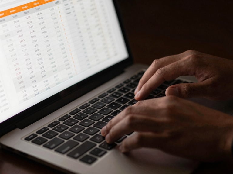 Close-up of hands working on a laptop with financial spreadsheets, highlighting a section with orange accents, sharp high-contrast lighting, deep charcoal and vibrant orange tones, professional editorial style, 35mm, focused on data.