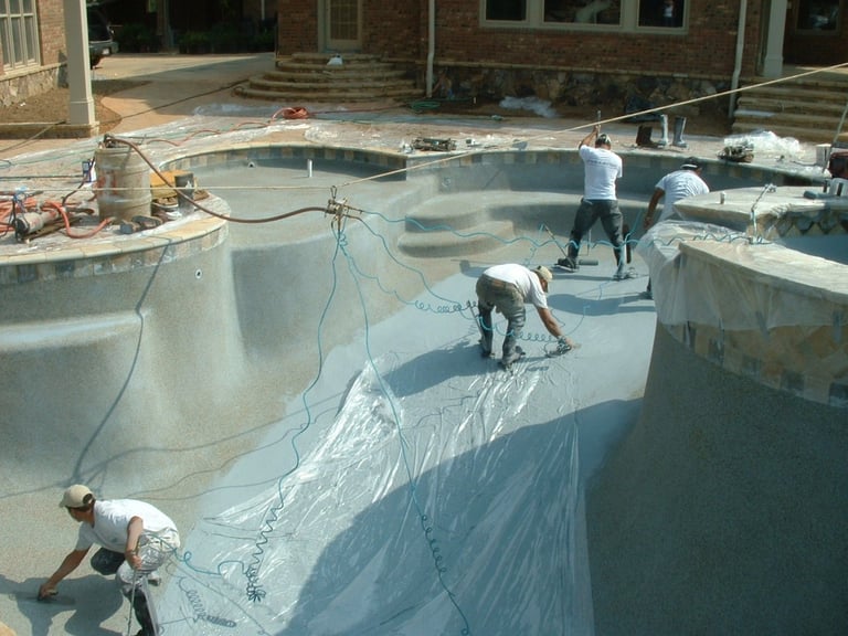Professional pool contractors applying a gray plaster finish during a luxury backyard swimming pool renovation.