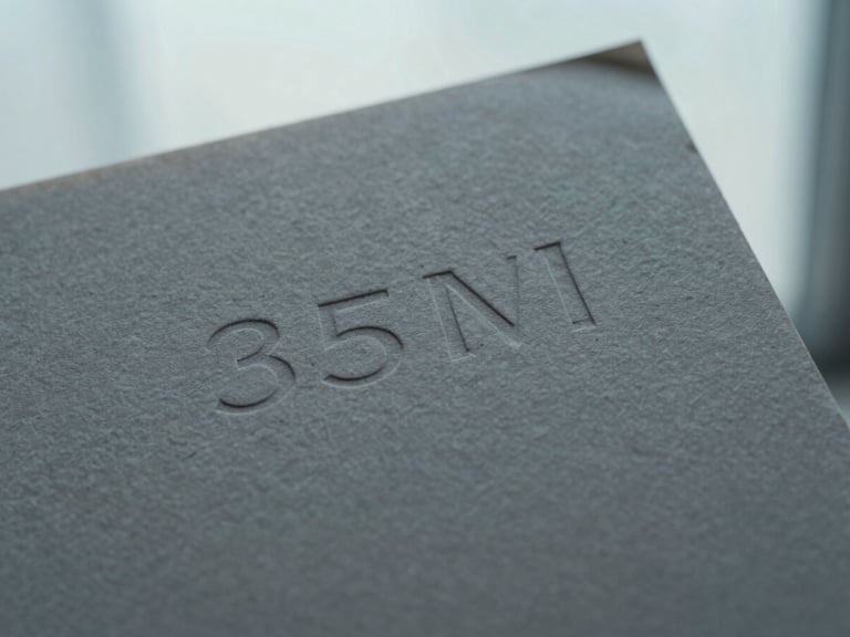 Macro close-up of premium textured gray paper stock with embossed minimalist typography, soft diffused window light, 35mm.
