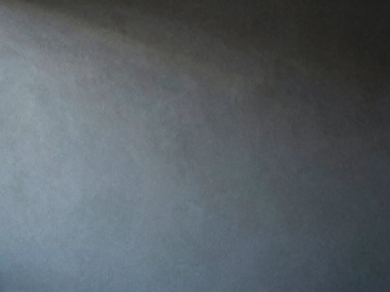 Abstract composition of light and shadow on a matte plaster wall, minimalist interior detail, muted charcoal and soft blue tones, 35mm.