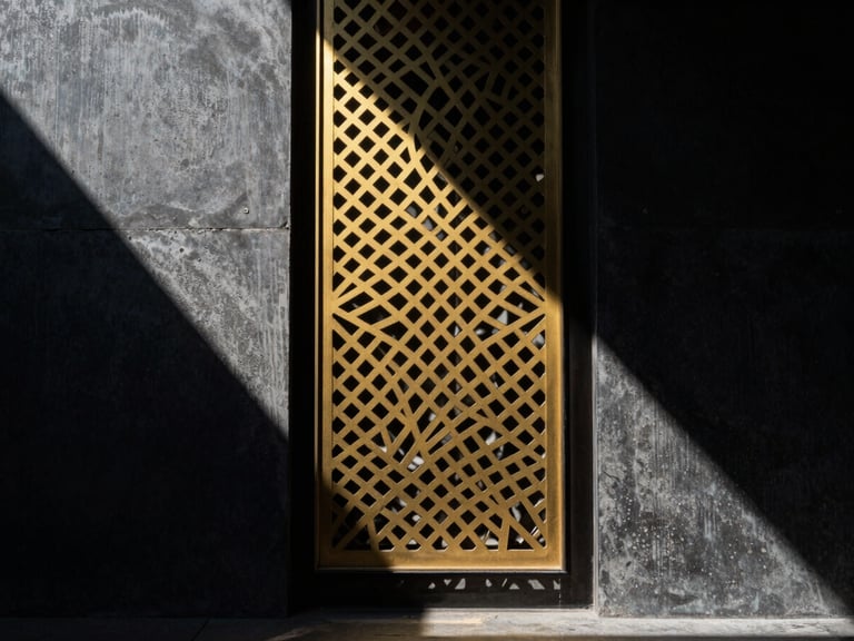 Dramatic architectural photography of a golden laser-cut metal screen casting geometric shadows on a dark concrete wall, high contrast directional sunlight, 35mm