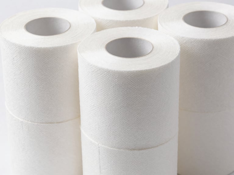 Macro close-up of a stack of large, commercial-grade tissue paper rolls, uniformly white, bright clinical studio light, sterile white background.