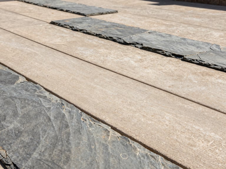 Macro architectural shot of a stamped slate patio finish, warm concrete and slate tones, crisp shadows under bright direct sunlight.