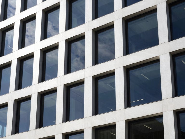 Sleek office building facade with tinted windows, crisp clean-room white light, reflecting a clear sky.
