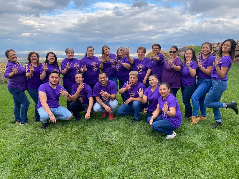 A large group of people wearing purple t-shirts posing on a grassy hill for awareness.