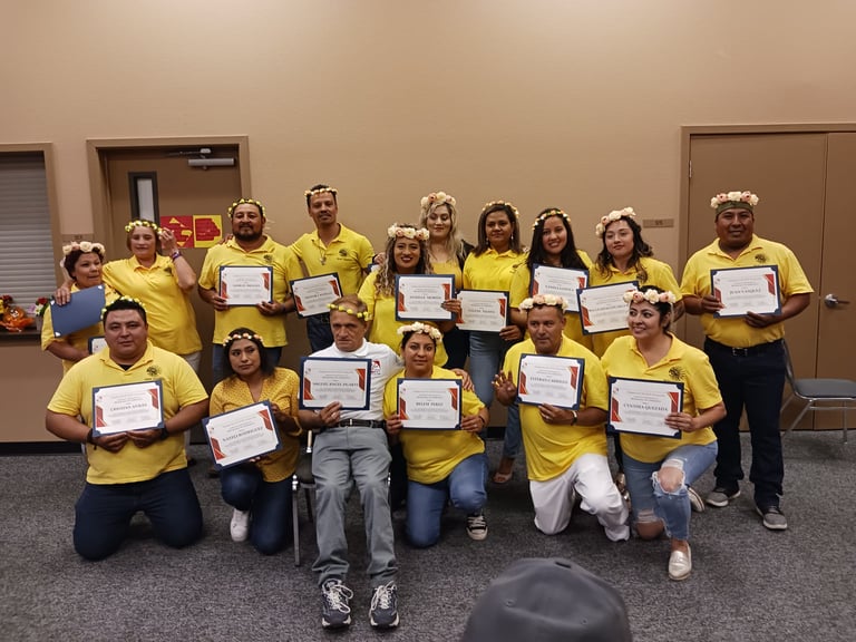 A group of diverse graduates in yellow shirts posing with their certificates at a graduation ceremony.