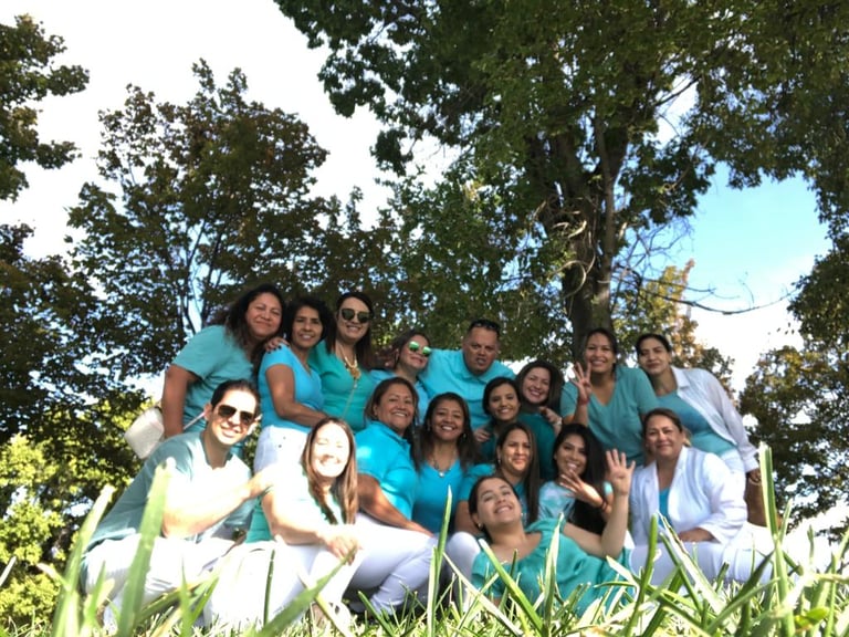 A smiling dental staff group photo outdoors wearing teal scrubs and white pants for a team building event.
