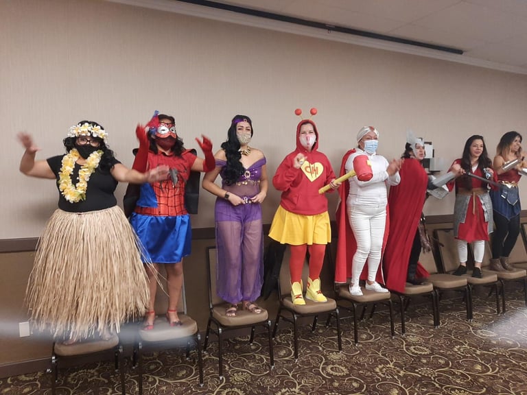 Diverse group in Halloween costumes including a hula dancer, Spider-Man, and Wonder Woman at an office party.