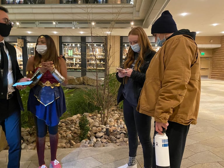 A woman in a Wonder Woman costume and face mask stands with a group in a shopping mall.