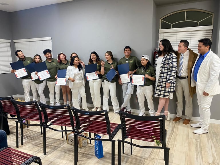 Smiling group of graduates in green polo shirts holding certificates at a formal recognition ceremony.
