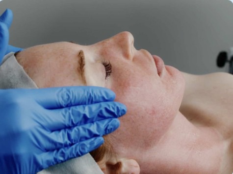 patient laying while doctor with blue gloves on massages her temples