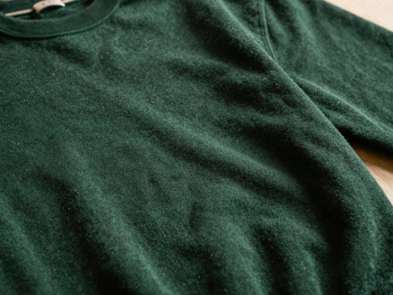 Close-up of a heavy cotton sweatshirt fabric, deep forest green, with subtle texture visible under warm, dramatic side-lighting, shallow depth of field.