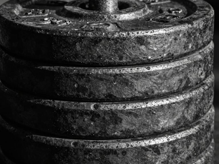 Extreme close-up of a stack of heavy iron weight plates, black and white, high contrast, textured metal, with harsh side lighting creating deep shadows.