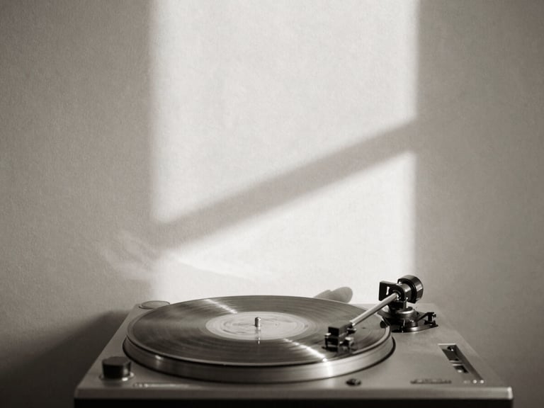 Minimalist black and white photography of a single vinyl record spinning on a turntable, soft natural window light casting long shadows on a cream plaster wall, sepia undertones