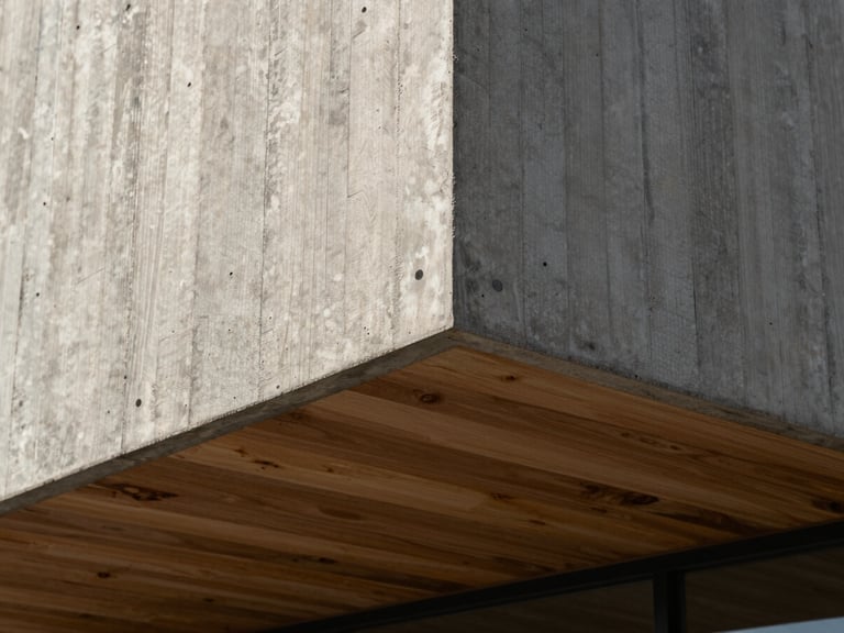 A close-up geometric detail of a modern concrete and timber facade under bright natural daylight, highlighting rich wood grain and raw concrete texture.