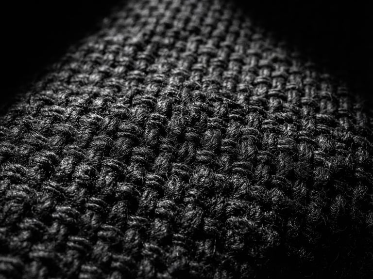 Extreme close-up of heavy black cotton fabric weave, high-contrast directional light creating sharp shadows, minimalist studio setting, 35mm