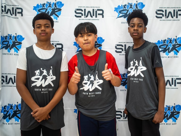 Three young basketball players in SWR South West Runs jerseys posing at a sports community event.
