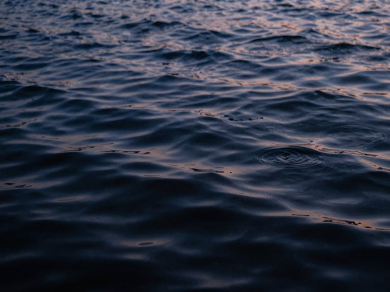 Close-up of rippling water surface at dusk, deep indigo and slate tones, moody film photography, shallow depth of field.