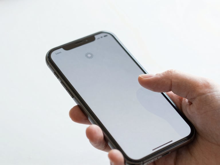 Close-up of a hand gently touching a smartphone screen that shows a loading spinner or a frozen app, conveying a common problem, bright natural daylight, 35mm.