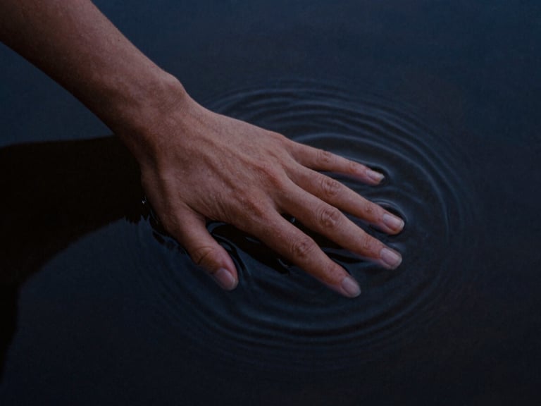 Close-up of a single hand tracing ripples in dark, still water, soft chiaroscuro, midnight blue tones, 35mm film