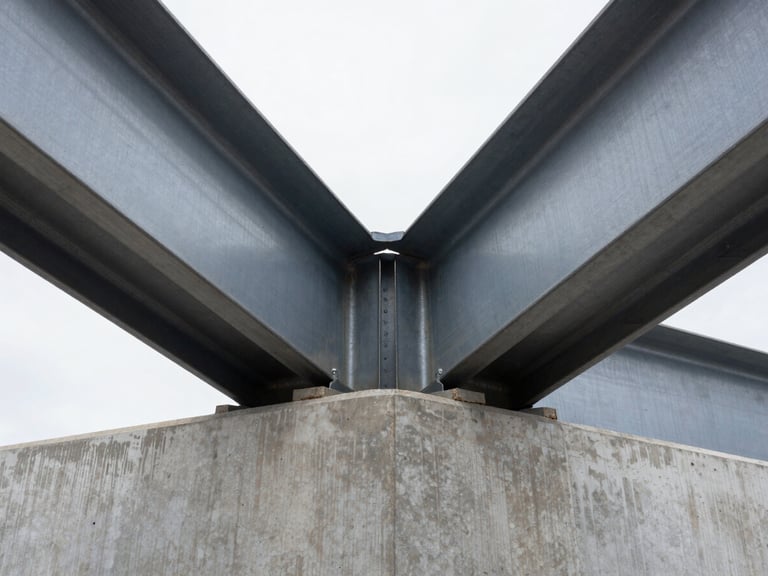 Symmetrical close-up of heavy structural steel beams meeting a site-poured concrete foundation, high-contrast overcast daylight emphasizing the raw metallic and concrete textures.