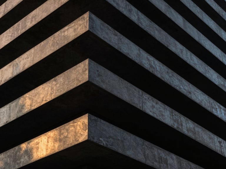 Dramatic structural angle of a premium modern building facade, monolithic dark concrete, sharp architectural lines, golden hour highlights