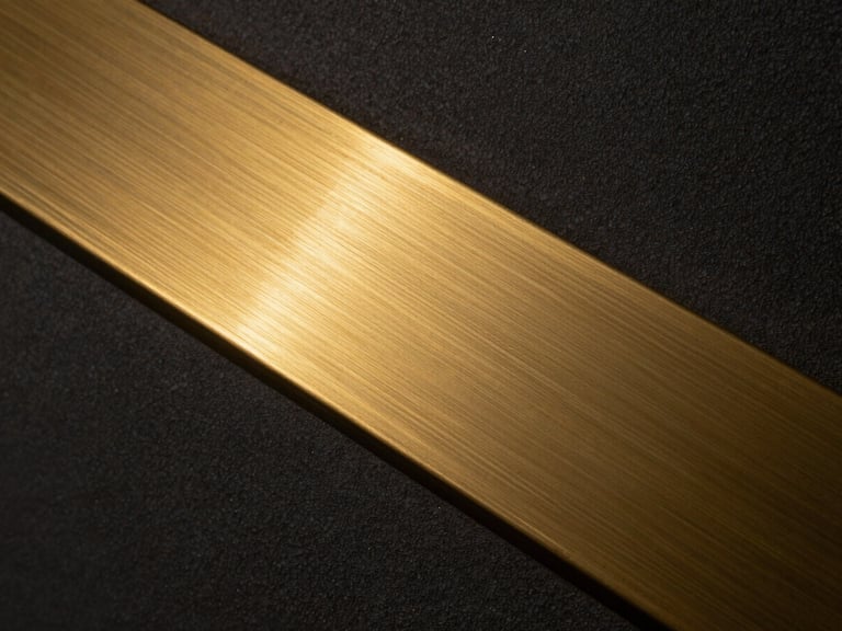 Extreme close-up of a brushed brass inlay transitioning into dark textured plaster, low-key lighting, metallic gold glints, ultra-high resolution