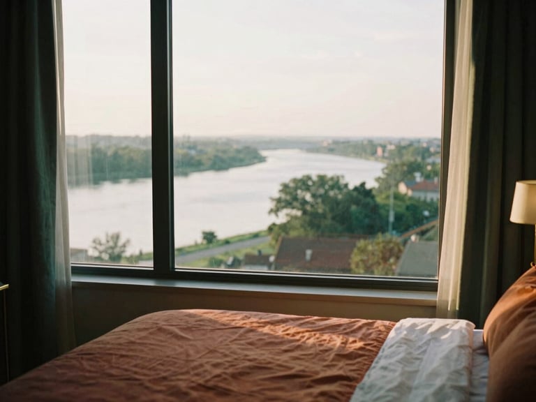 Top floor homestay room with wide river view from window, golden hour light, cozy bed, brass accents, shallow depth of field, 35mm film