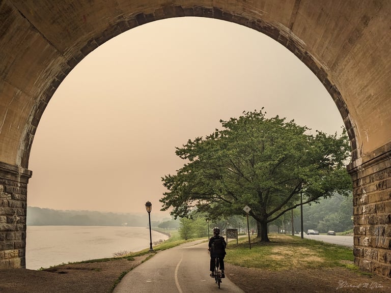 Cyclist faces a yellow haze along a river trail