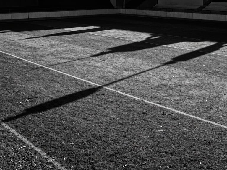 An empty regional football pitch in Seville under a late afternoon sun, long dramatic shadows, high-contrast black and white, 35mm film grain