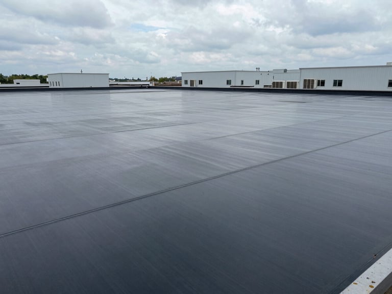 Wide aerial view of a flat commercial rooftop membrane installation, overcast daylight, HVAC units visible in background, clean seam lines in foreground, no people, honest documentary framing