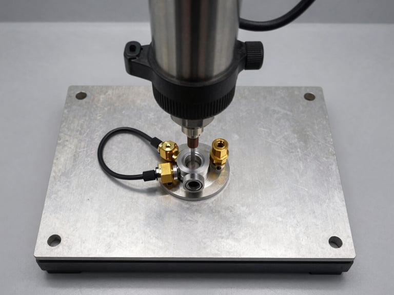 Overhead flat-lay shot of a press-fit and leak-test machine fixture plate, hydraulic press cylinder above, air-decay test fittings connected to component port, crisp overhead shop-floor task lighting, steel and aluminium components sharp in frame