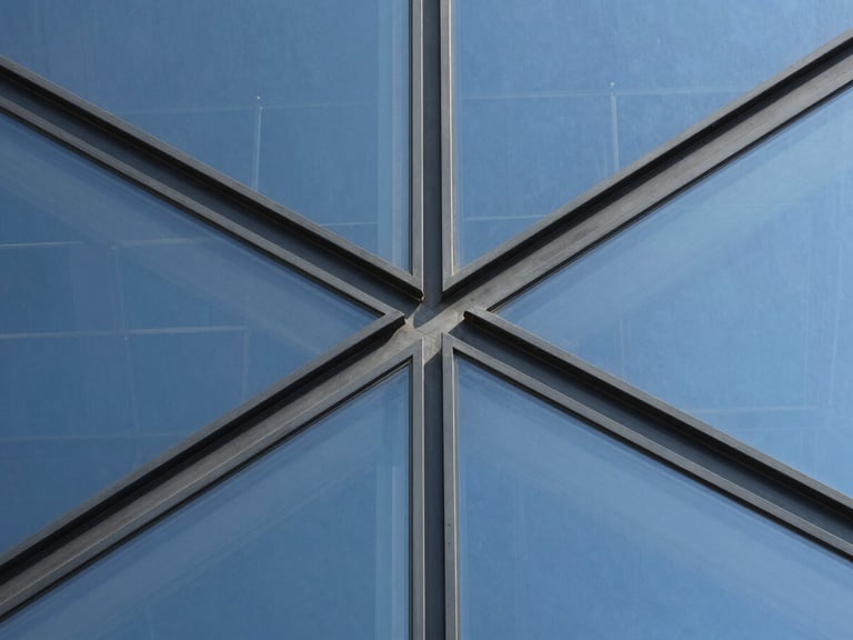 Extreme macro detail of a structural glass curtain wall joint, showing precise metal connections and reflective surfaces under sharp daylight.