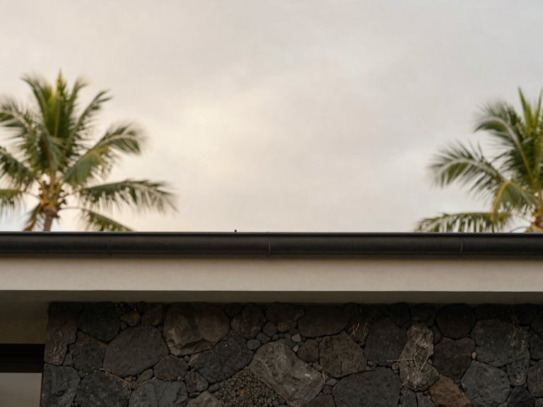 Architectural detail of a minimalist villa roofline and rain gutter against a soft, overcast tropical sky, clean lines, volcanic stone wall