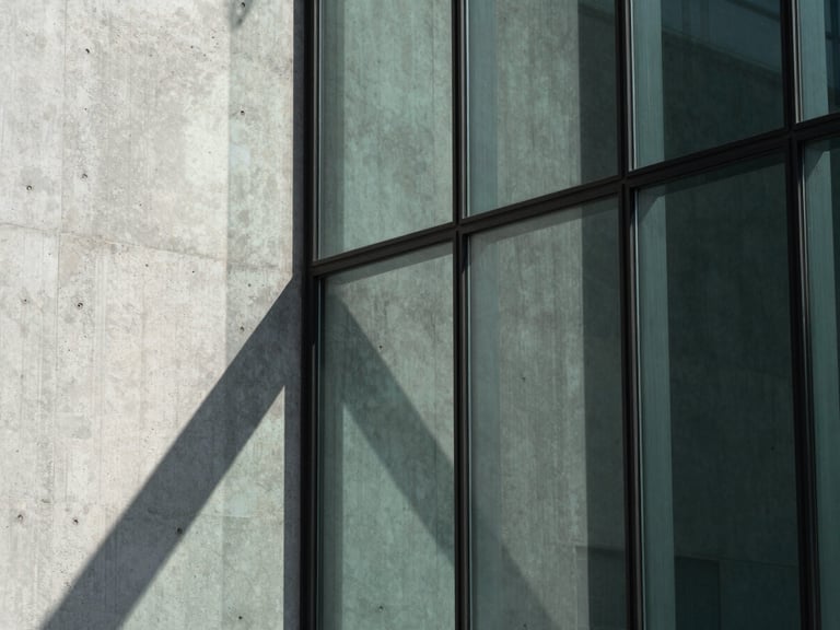 Macro detail of high-performance architectural glazing with sharp daylight shadows, concrete and glass textures, desaturated green accents.