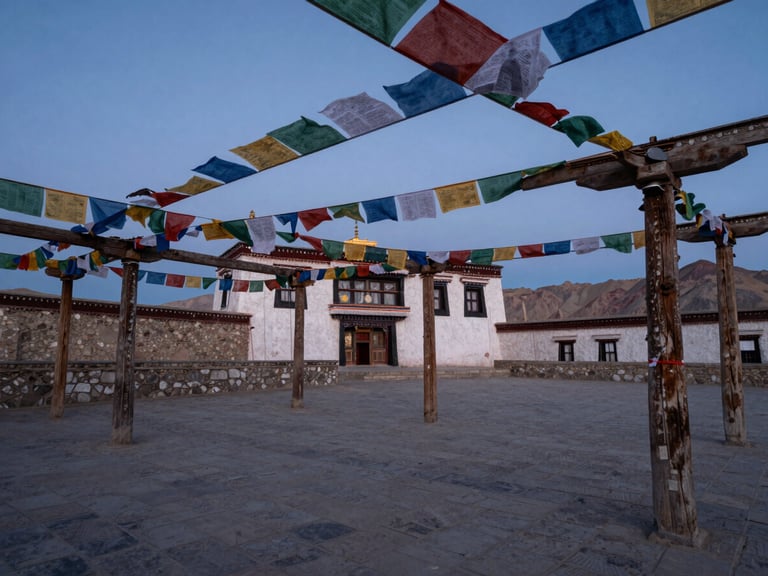 An ancient stone monastery courtyard in Ladakh at dusk, soft blue-hour light, prayer flags gently fluttering, weathered wooden pillars, serene negative space