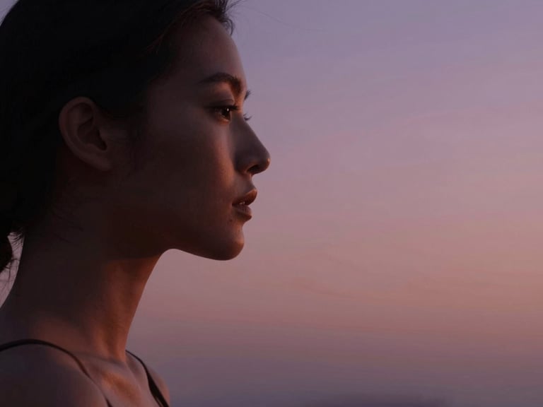 Retrato íntimo y sereno de una persona en un momento de introspección, perfil suavemente iluminado por luz natural de atardecer, con sombras tenues que aportan profundidad. Encuadre cerrado de detalle con amplio espacio negativo. Warm editorial photography, soft golden-hour light, dusty pink and deep purple tones, elegant minimalist composition, 35mm.