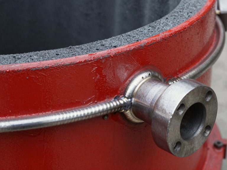 Close-up of welded flanges on a heavy-duty red painted steel foam chamber, visible weld seams, sharp industrial lighting