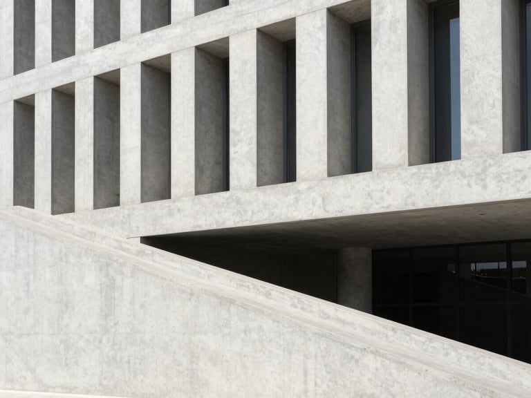 Modern concrete building facade with a clean accessible ramp integrated into the landscape, bright sunlight, sharp geometric lines