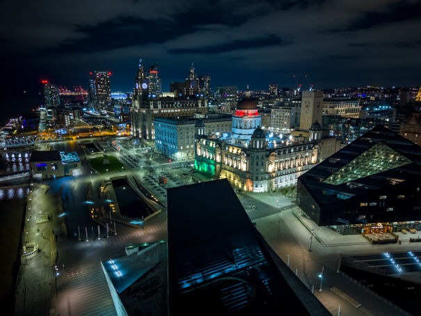 Aerial night view of Liverpool waterfront featuring the Port of Liverpool Building and city skyline.