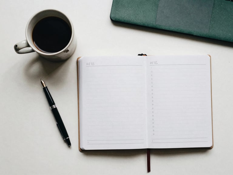 Overhead flat-lay of a clean study desk with a ceramic coffee cup, a fountain pen, and a neat open planner, soft daylight