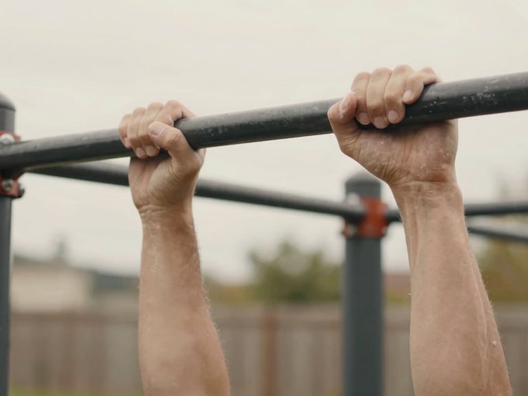 Candid close-up of chalked hands gripping a black steel pull-up bar in a backyard, natural overcast daylight, 35mm.